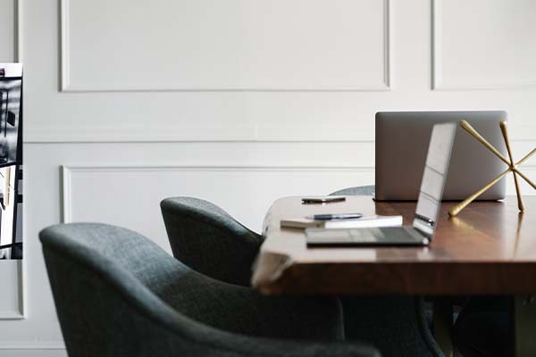 A modern business law office conference room with a wooden table, gray upholstered chairs, and an open laptop against a white paneled wall.