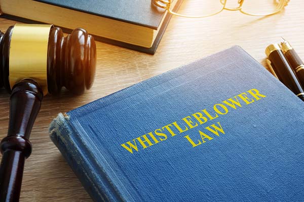 A blue book titled Whistleblower Law in gold lettering next to a judge's gavel and reading glasses on a wooden desk.
