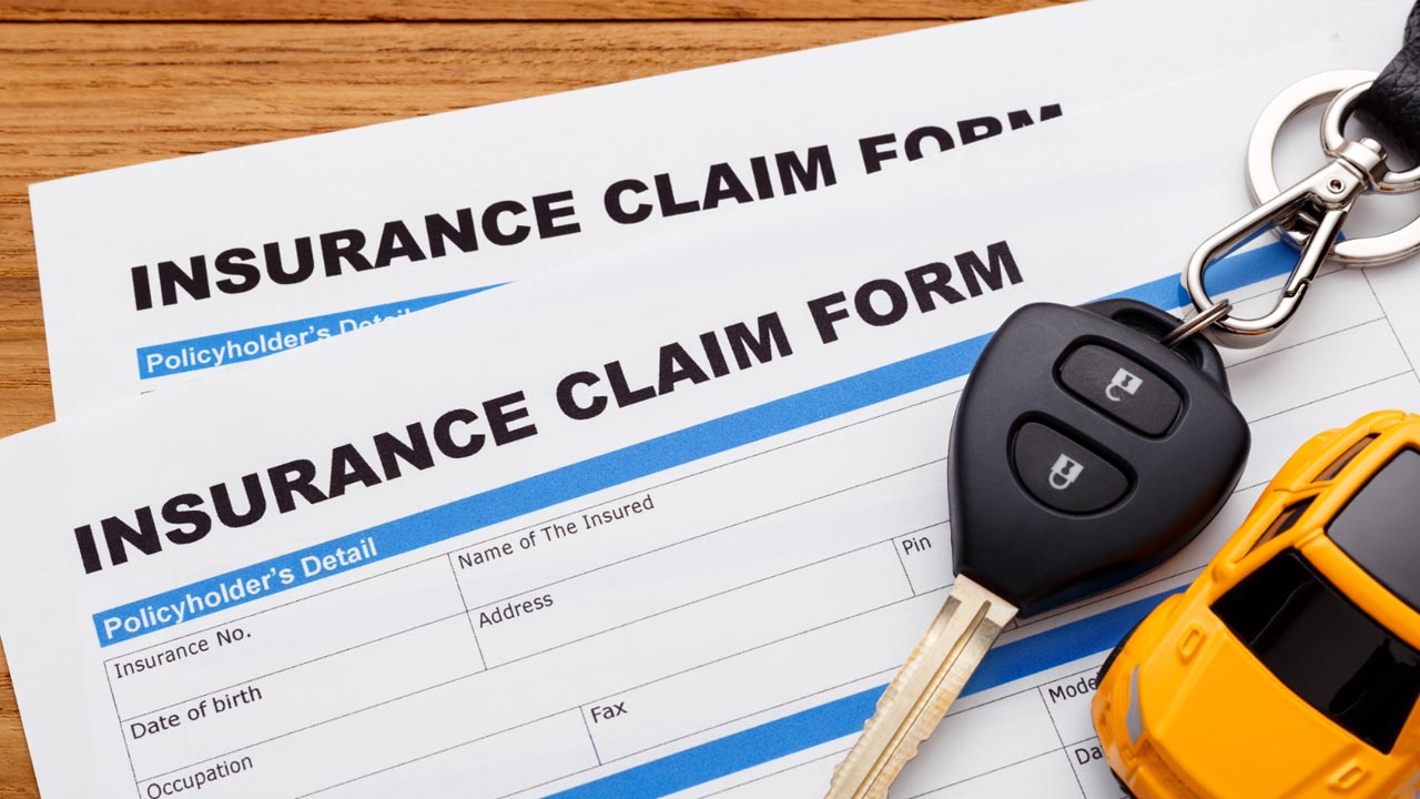 Two blank auto insurance claim forms on a wooden desk with a car key and a small model car resting on top, representing a Texas auto accident insurance claim.