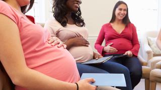 Three pregnant women sitting together in a bright, comfortable room, smiling and holding their bellies during a prenatal class or group meeting that symbolizes a palsy lawyer for birth injury cases.